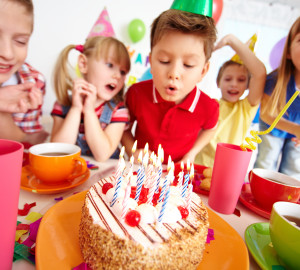 Group of adorable kids looking at birthday cake with candles, cute boy blowing on them
