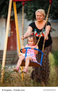 Grandmother pushing granddaughter on swing in park