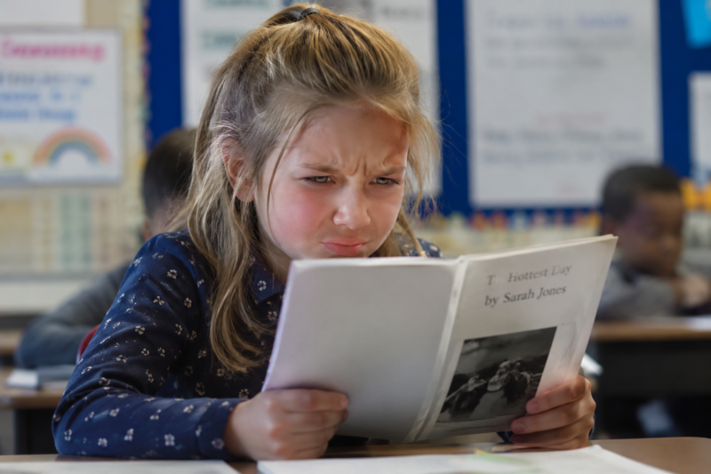 Little girl frustrated as she tries to read a book.